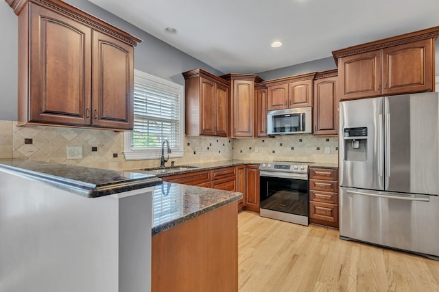 308 Stanley Park Ln, Franklin, TN 37069 - kitchen with stainless steel appliances, a sink, a peninsula, dark stone countertops, and light wood-style flooring