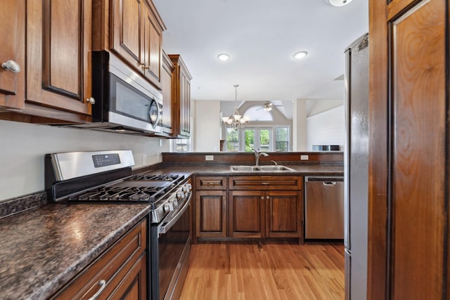 kitchen with stainless steel appliances, a sink, dark countertops, light wood finished floors, and pendant lighting