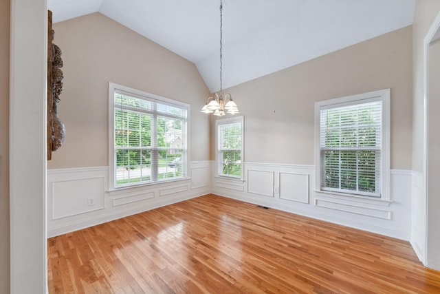 unfurnished room featuring light wood-style flooring, a wainscoted wall, a chandelier, and lofted ceiling