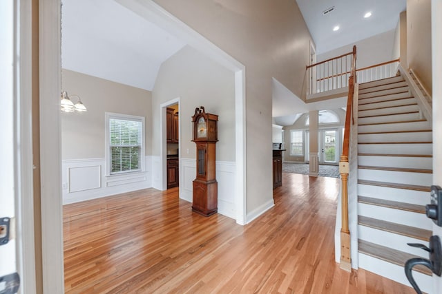 entrance foyer featuring healthy amount of natural light, light wood-style flooring, stairs, a wainscoted wall, and high vaulted ceiling