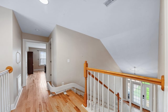 hall featuring an upstairs landing, light wood-style floors, baseboards, and vaulted ceiling