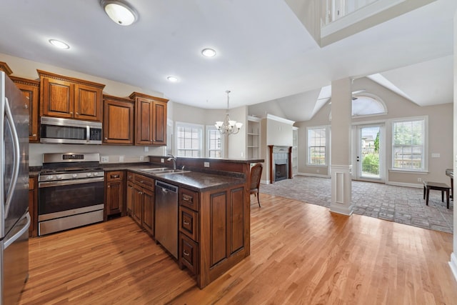kitchen with stainless steel appliances, a sink, open floor plan, a peninsula, and light wood finished floors