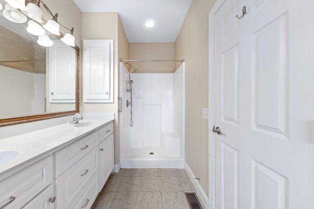 bathroom featuring a shower, double vanity, tile patterned flooring, and baseboards