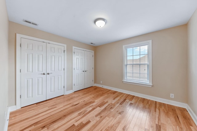 unfurnished bedroom featuring two closets, baseboards, and light wood finished floors