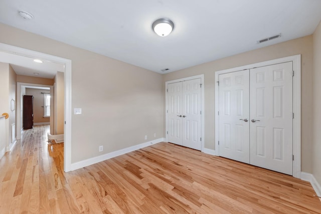 unfurnished bedroom featuring multiple closets, light wood finished floors, and baseboards