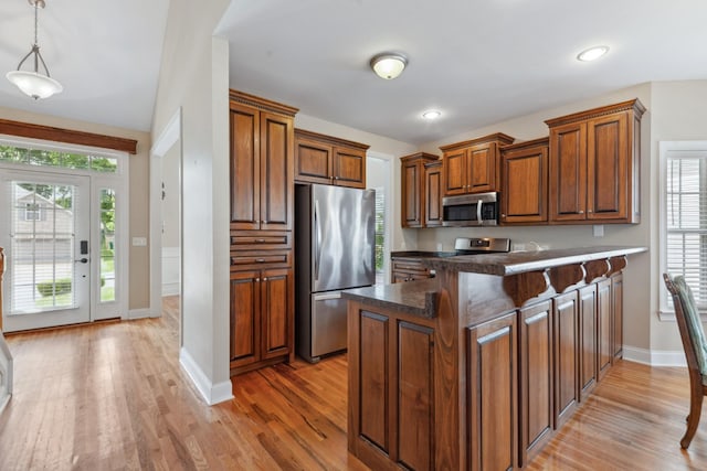 kitchen with appliances with stainless steel finishes, a peninsula, light wood-style flooring, brown cabinetry, and recessed lighting