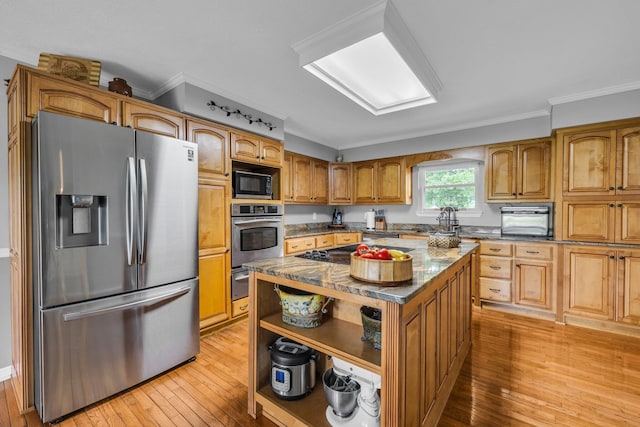 kitchen with black appliances, light wood-style flooring, ornamental molding, a center island, and dark stone countertops
