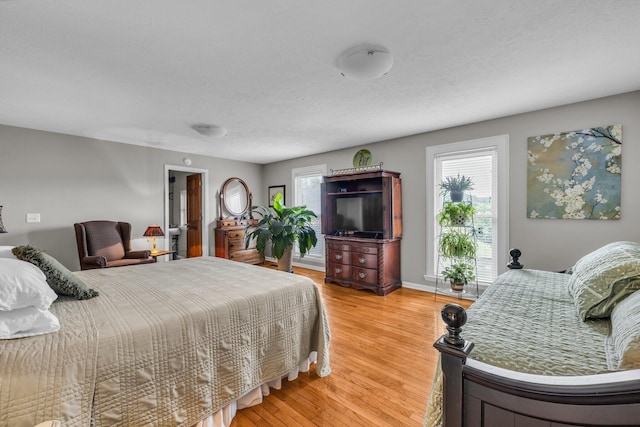 bedroom featuring light wood-style flooring, baseboards, and a textured ceiling