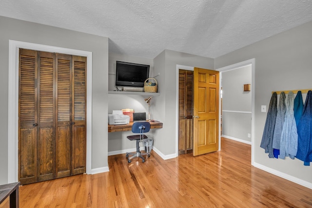 bedroom featuring light wood finished floors, multiple closets, baseboards, and a textured ceiling