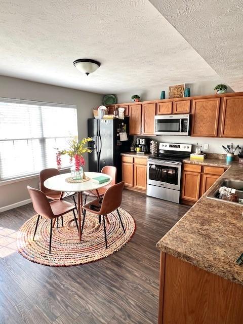 1011 Wolves Den Pl, Murfreesboro, TN 37128 - kitchen featuring stainless steel appliances, brown cabinets, a textured ceiling, dark wood-style floors, and baseboards
