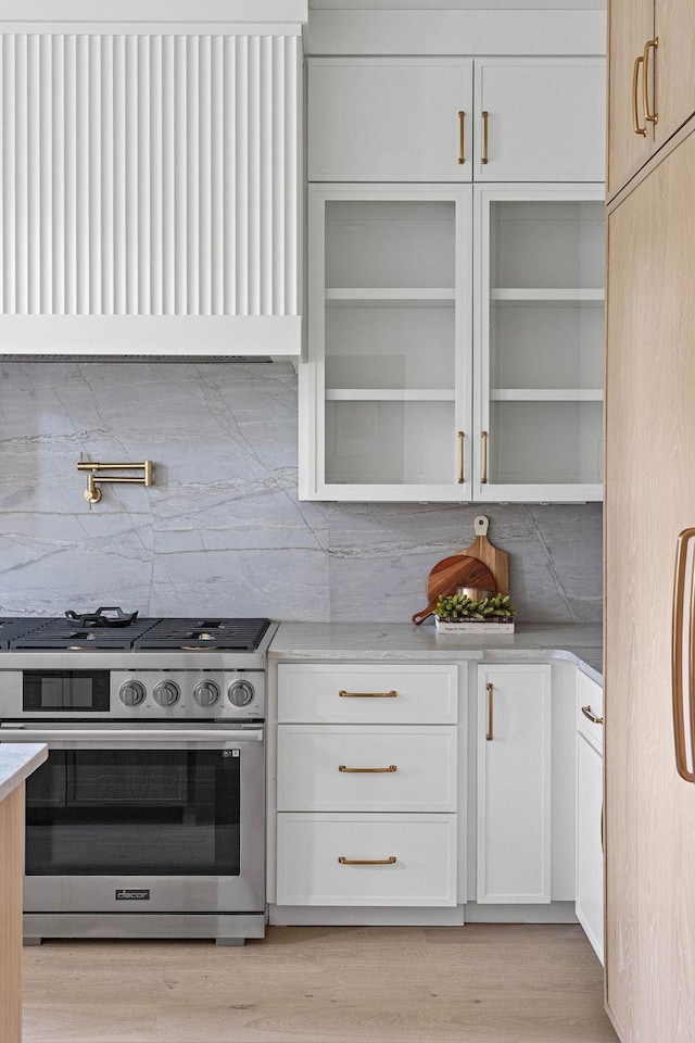 219 Chamberlin St, Nashville, TN 37209 - kitchen with stainless steel range with gas stovetop, ventilation hood, tasteful backsplash, white cabinetry, and light wood finished floors