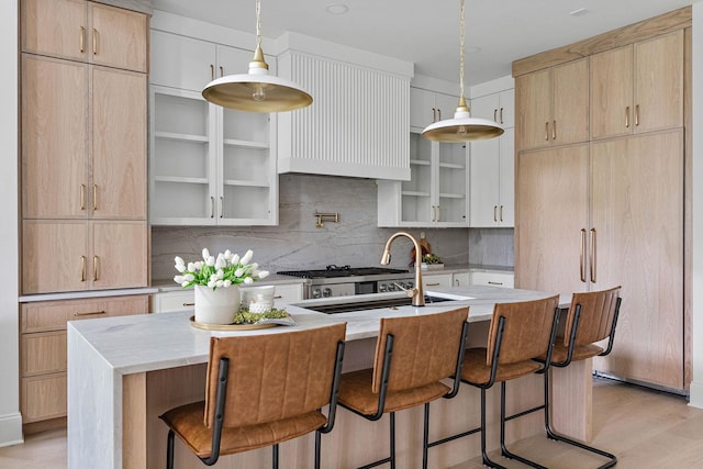 219 Chamberlin St, Nashville, TN 37209 - kitchen featuring backsplash, light wood-style floors, a center island with sink, a kitchen breakfast bar, and light stone counters