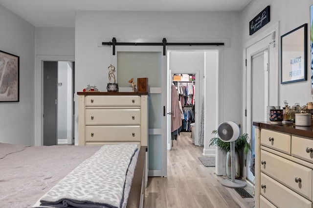 bedroom with light wood finished floors, a walk in closet, and a barn door