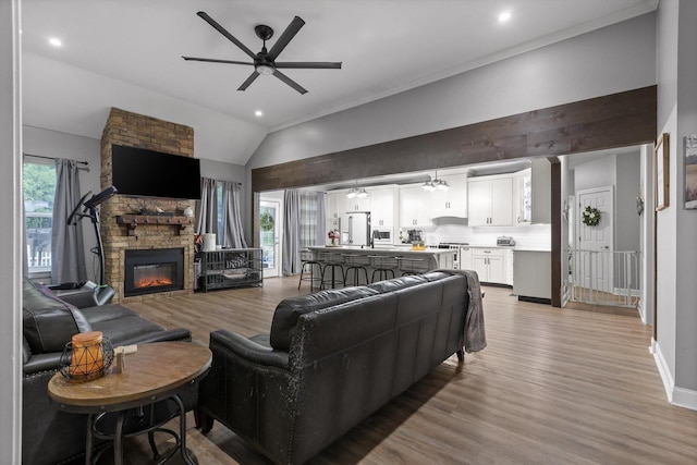living area with a ceiling fan, lofted ceiling, light wood-style flooring, a stone fireplace, and recessed lighting