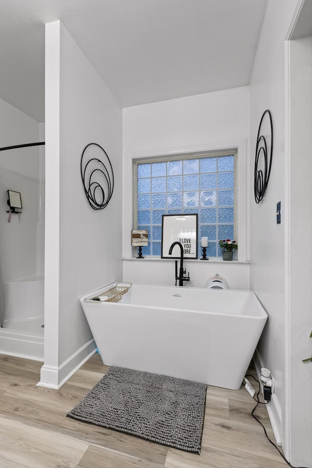 bathroom featuring baseboards, wood finished floors, a soaking tub, and a shower