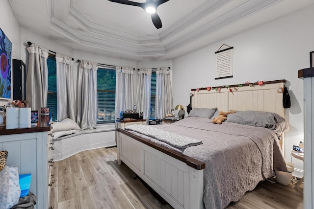 bedroom featuring ornamental molding, light wood-type flooring, a tray ceiling, and ceiling fan