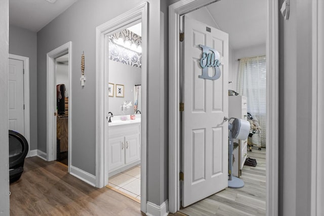 corridor featuring light wood-type flooring, baseboards, and a sink