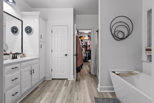 bathroom featuring wood finished floors, a freestanding bath, vanity, a spacious closet, and baseboards
