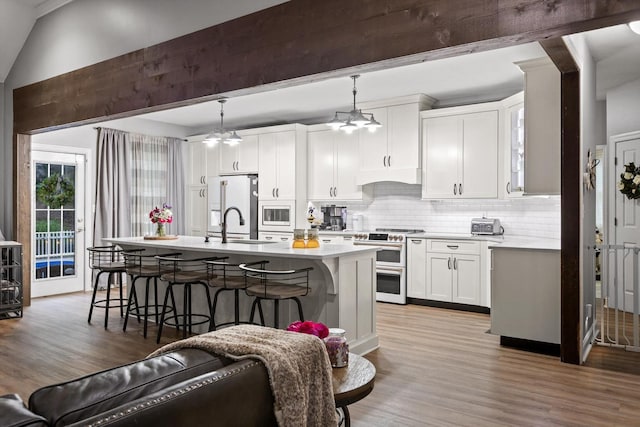 kitchen with white appliances, a center island with sink, wood finished floors, under cabinet range hood, and vaulted ceiling