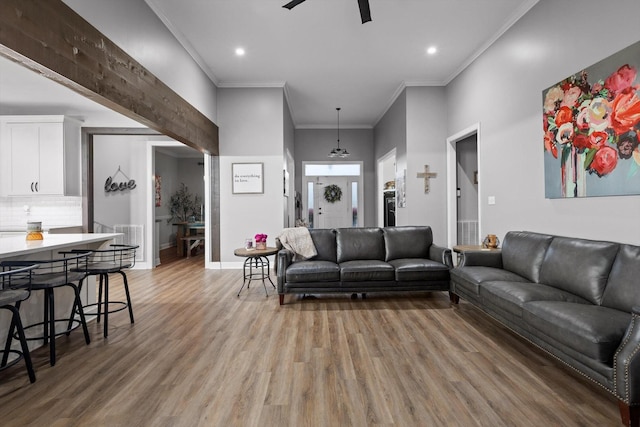 living room featuring light wood-style floors, a ceiling fan, baseboards, ornamental molding, and recessed lighting