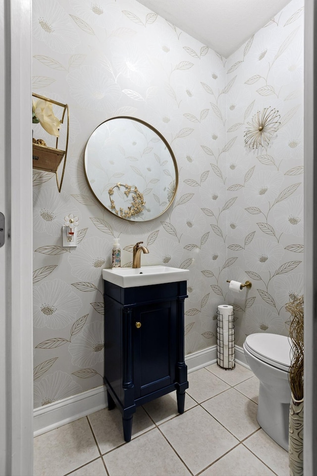 half bathroom with baseboards, wallpapered walls, tile patterned flooring, toilet, and vanity