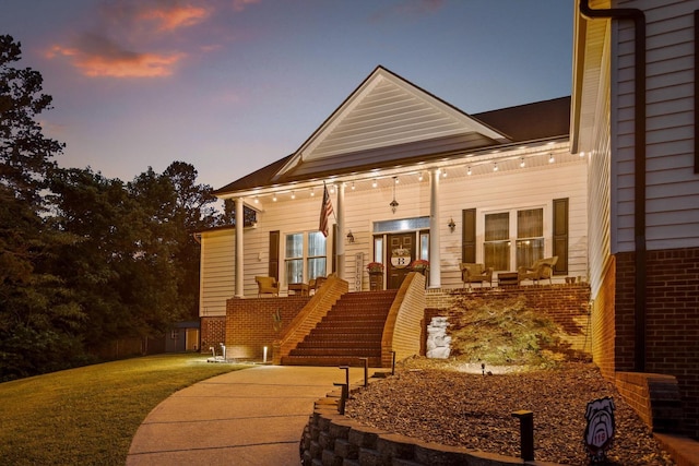 view of front of property featuring brick siding, covered porch, and a yard