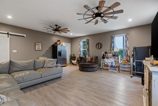 living room featuring a barn door, a ceiling fan, light wood-type flooring, and recessed lighting