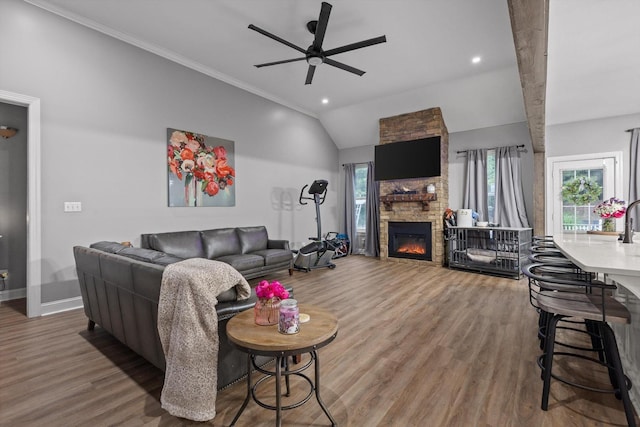 living area with a ceiling fan, wood finished floors, a stone fireplace, vaulted ceiling, and baseboards