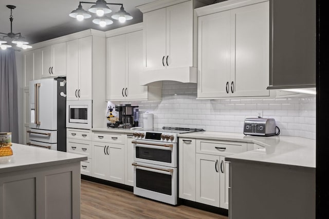 kitchen with white appliances, under cabinet range hood, light countertops, a chandelier, and white cabinets