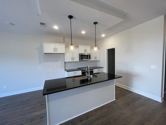 53 Charleston Cv, Clarksville, TN 37043 - kitchen with stainless steel microwave, dark countertops, white cabinets, dark wood-style flooring, and a center island with sink