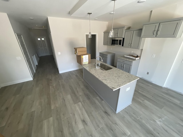 56 Charleston Cv, Clarksville, TN 37043 - kitchen featuring stainless steel microwave, gray cabinetry, light wood-style floors, an island with sink, and light stone counters