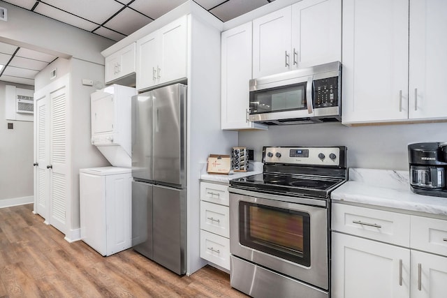 105 W Walnut St, Smithville, TN 37166 - kitchen featuring appliances with stainless steel finishes, stacked washer and clothes dryer, a drop ceiling, light wood-style floors, and white cabinetry