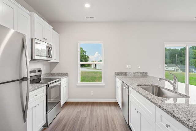 2028 Lala Loop, White Bluff, TN 37187 - kitchen with stainless steel appliances, a sink, light wood-style floors, white cabinetry, and light stone countertops