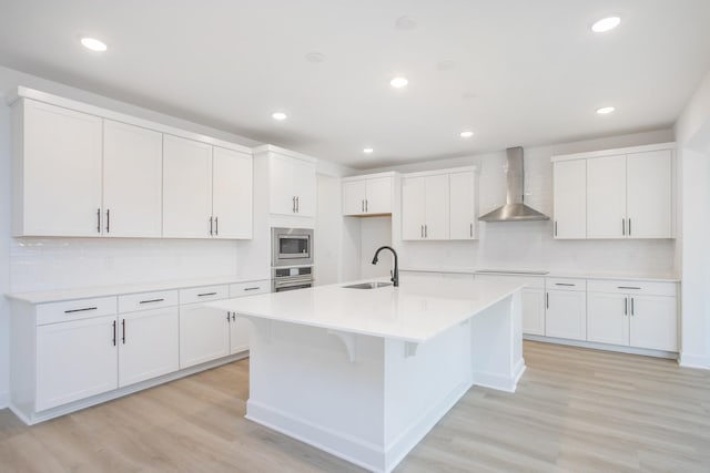 133 W Cassa Way, Mount Juliet, TN 37122 - kitchen featuring wall chimney exhaust hood, stainless steel appliances, a sink, an island with sink, and light wood-style floors
