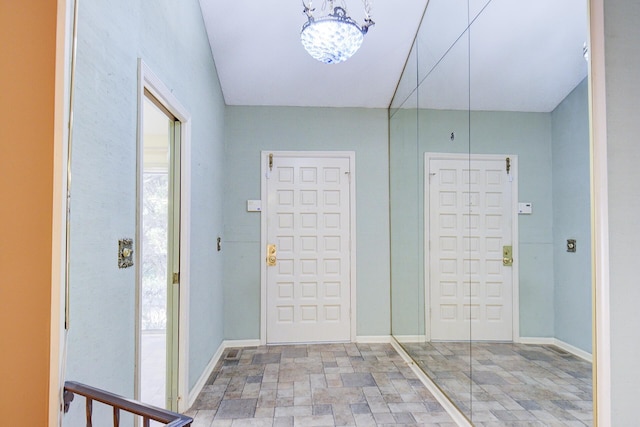 entrance foyer with stone finish floors, a chandelier, and baseboards