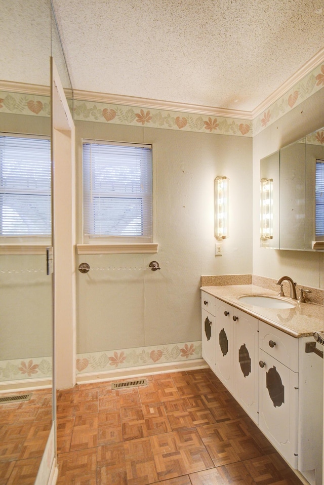 bathroom with a textured ceiling, healthy amount of natural light, ornamental molding, vanity, and baseboards
