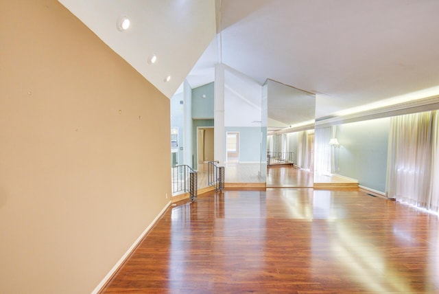 unfurnished living room featuring wood finished floors, baseboards, high vaulted ceiling, plenty of natural light, and recessed lighting