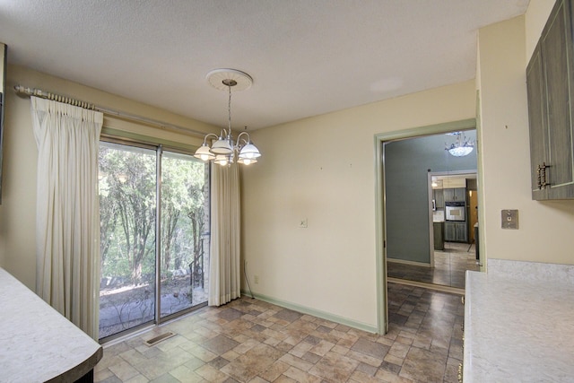 unfurnished dining area featuring stone tile flooring, a chandelier, and baseboards