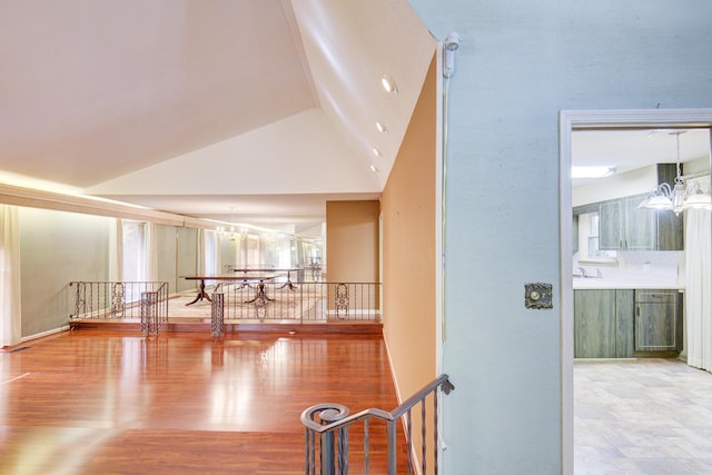 hallway with a chandelier, an upstairs landing, high vaulted ceiling, and wood finished floors