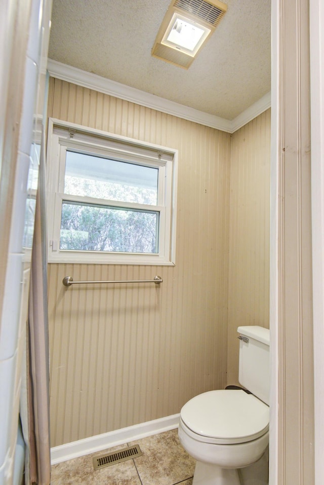 bathroom featuring toilet, crown molding, a textured ceiling, baseboards, and tile patterned flooring