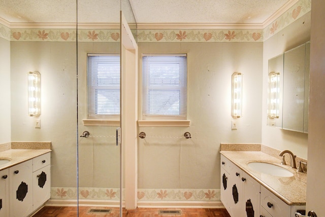 full bathroom with ornamental molding, two vanities, a shower with door, baseboards, and a textured ceiling