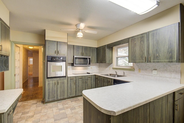 kitchen featuring appliances with stainless steel finishes, a sink, light countertops, decorative backsplash, and a ceiling fan