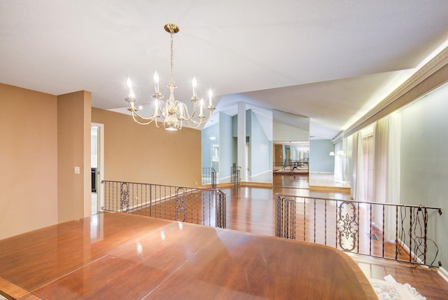 hall with a chandelier, an upstairs landing, vaulted ceiling, and wood finished floors