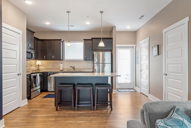 5008 Fennel Ct, Spring Hill, TN 37174 - kitchen with appliances with stainless steel finishes, dark brown cabinetry, a kitchen breakfast bar, light wood-type flooring, and light stone counters