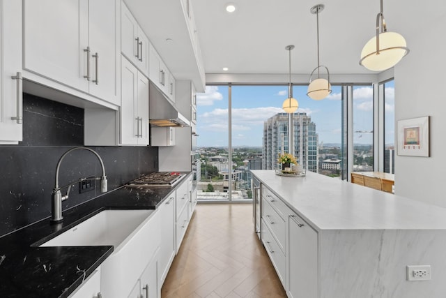 1616 W End Ave Unit 2008, Nashville, TN 37203 - kitchen featuring under cabinet range hood, stainless steel gas stovetop, white cabinets, decorative backsplash, and a kitchen island