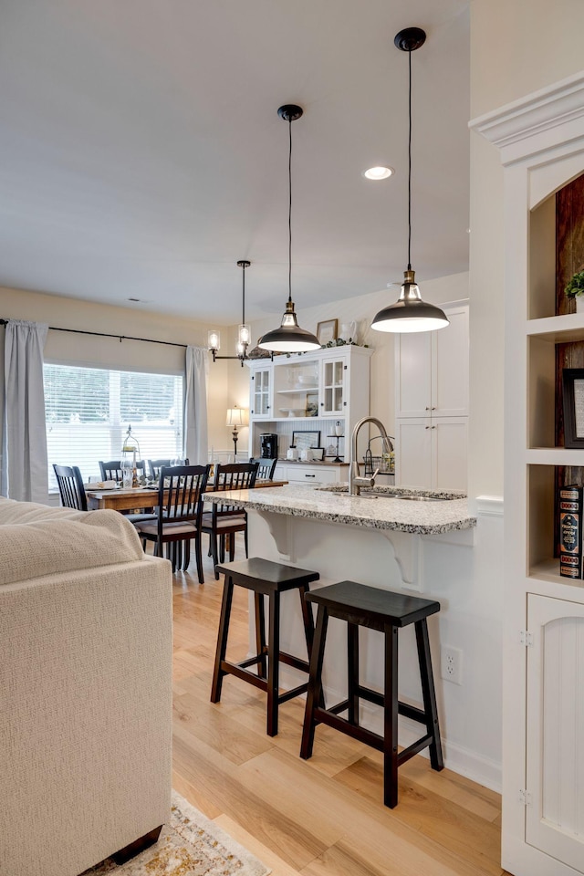 979 Carnation Dr, Spring Hill, TN 37174 - kitchen featuring white cabinetry, glass insert cabinets, a breakfast bar, light stone countertops, and a peninsula