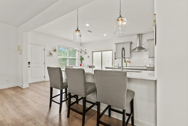 400 Parker Ct, Antioch, TN 37013 - kitchen with wall chimney exhaust hood, a kitchen breakfast bar, backsplash, light wood-type flooring, and decorative light fixtures