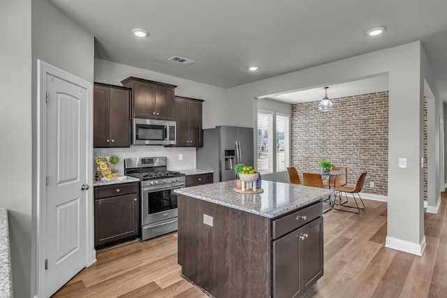 1010 Keeneland Dr, Spring Hill, TN 37174 - kitchen with stainless steel appliances, light wood finished floors, dark brown cabinetry, a center island, and brick wall