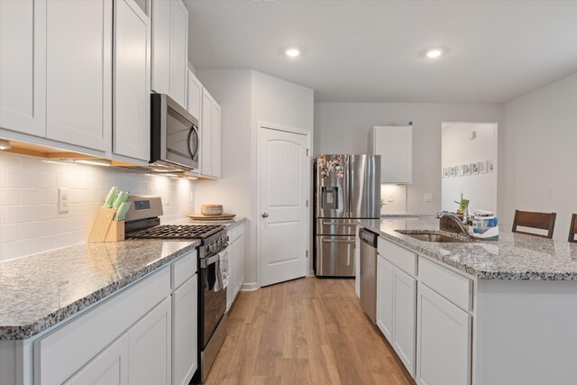2405 Quinn Dr, White House, TN 37188 - kitchen with appliances with stainless steel finishes, a sink, light wood-type flooring, decorative backsplash, and a center island with sink