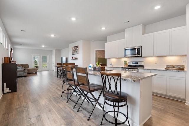 2405 Quinn Dr, White House, TN 37188 - kitchen with stainless steel appliances, decorative backsplash, light wood-type flooring, a breakfast bar area, and light stone counters
